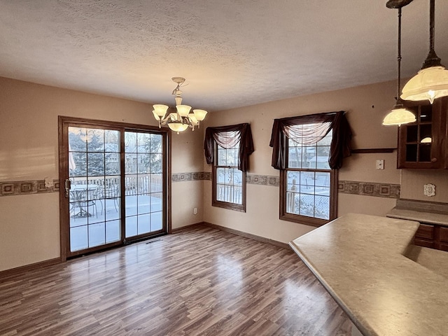 unfurnished dining area featuring a chandelier, a textured ceiling, dark wood finished floors, and baseboards