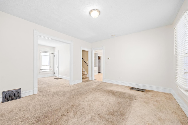 unfurnished room featuring baseboards, stairs, visible vents, and light colored carpet