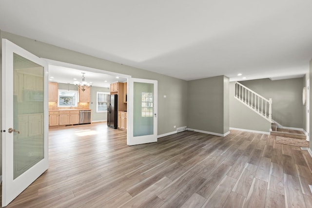 unfurnished living room featuring visible vents, stairway, wood finished floors, a chandelier, and baseboards