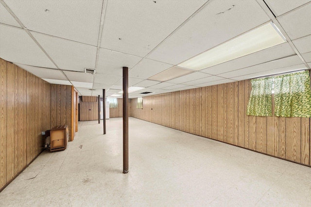 basement with a drop ceiling and wood walls