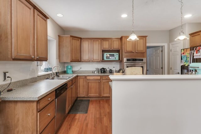 kitchen featuring appliances with stainless steel finishes, sink, light hardwood / wood-style floors, hanging light fixtures, and tasteful backsplash