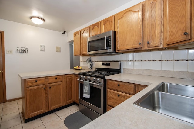 kitchen featuring light tile patterned flooring, appliances with stainless steel finishes, light countertops, a sink, and decorative backsplash