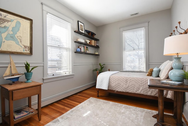 bedroom featuring multiple windows, a baseboard heating unit, and hardwood / wood-style floors