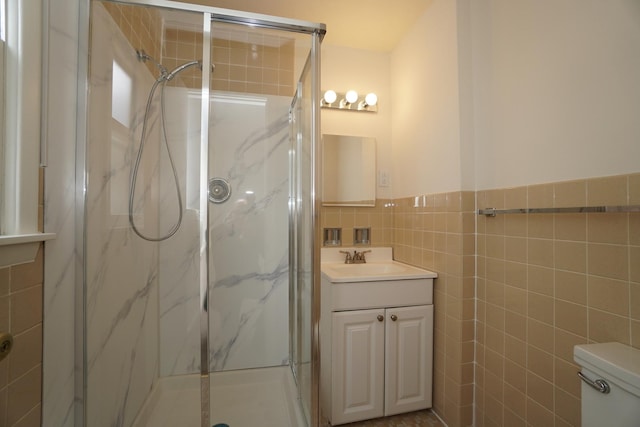 bathroom with toilet, vanity, tile walls, wainscoting, and a marble finish shower