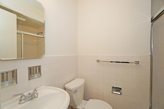 bathroom featuring tile walls, a sink, toilet, and a shower with door
