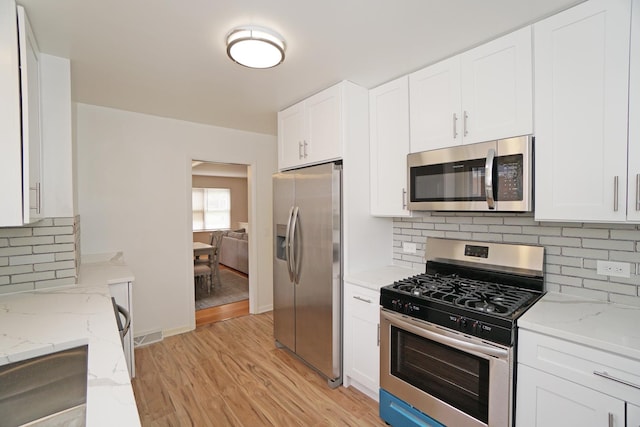 kitchen featuring stainless steel appliances, white cabinets, and light stone counters