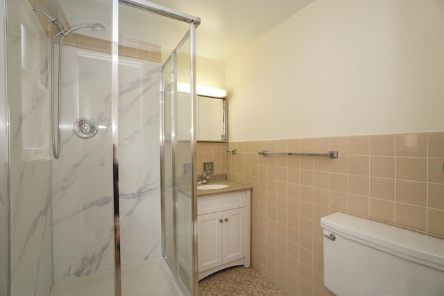 bathroom featuring toilet, a wainscoted wall, vanity, tile walls, and a marble finish shower