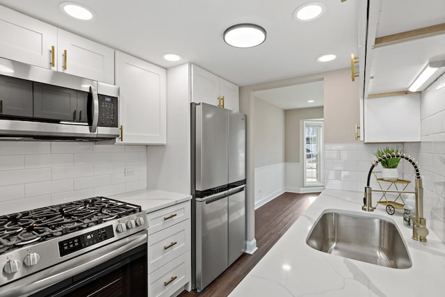 kitchen with appliances with stainless steel finishes, light stone countertops, white cabinets, dark hardwood / wood-style flooring, and sink