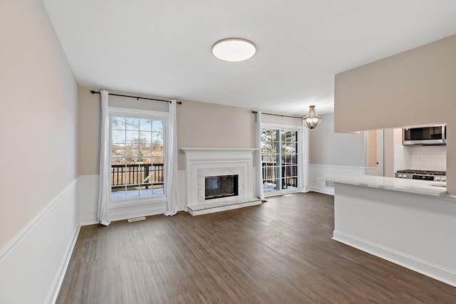 unfurnished living room with a notable chandelier, a premium fireplace, and dark hardwood / wood-style floors