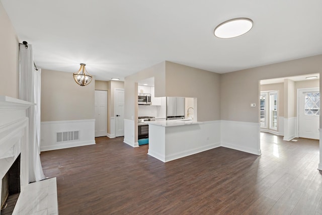 unfurnished living room with sink, a premium fireplace, dark hardwood / wood-style floors, and an inviting chandelier