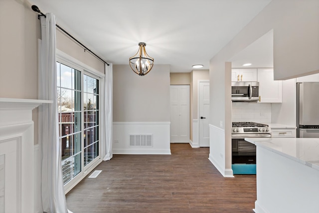 kitchen with appliances with stainless steel finishes, white cabinetry, pendant lighting, dark hardwood / wood-style flooring, and tasteful backsplash