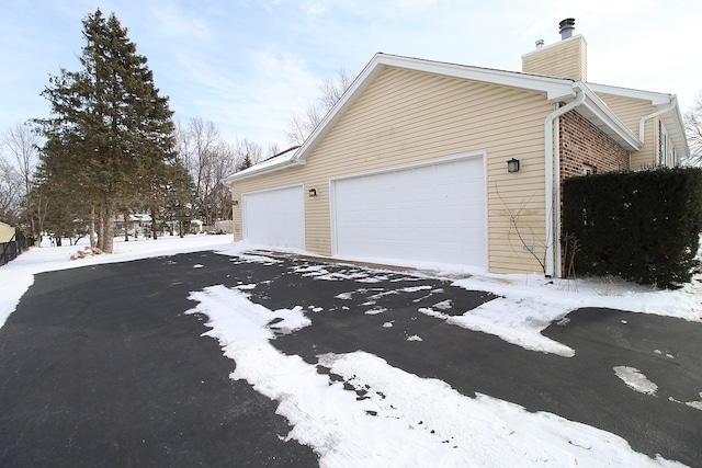 snow covered property with a garage, brick siding, and a chimney