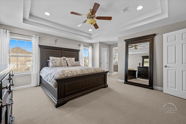 bedroom with a tray ceiling, ceiling fan, multiple windows, and light colored carpet