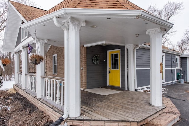 view of exterior entry featuring covered porch, brick siding, and roof with shingles