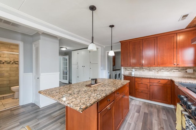 kitchen with a kitchen island, wood finished floors, decorative light fixtures, light stone countertops, and washing machine and dryer