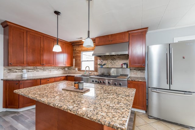 kitchen with light stone counters, pendant lighting, freestanding refrigerator, wall chimney range hood, and range