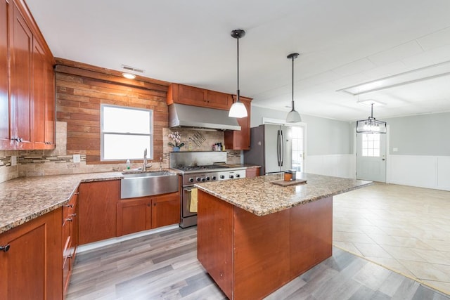 kitchen featuring wainscoting, a kitchen island, appliances with stainless steel finishes, range hood, and a sink