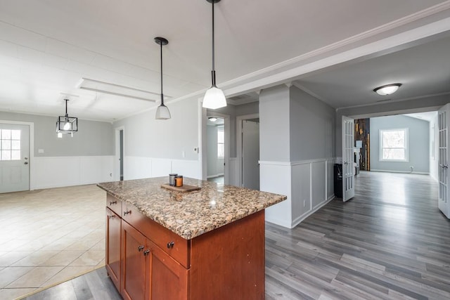 kitchen with decorative light fixtures, open floor plan, wainscoting, a kitchen island, and light stone countertops