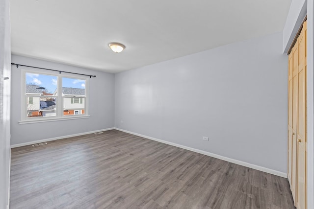 unfurnished bedroom with a closet, wood finished floors, visible vents, and baseboards