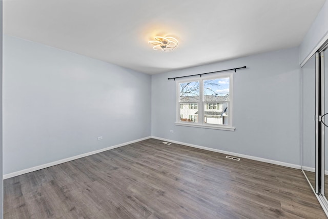 unfurnished bedroom with dark wood-style floors, a closet, visible vents, and baseboards