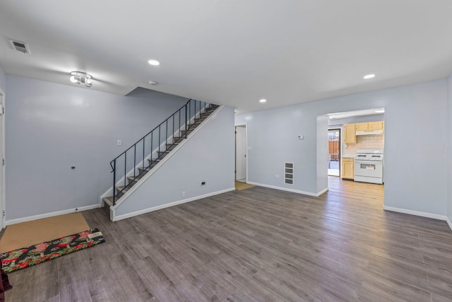 unfurnished living room with wood finished floors, visible vents, baseboards, and stairs