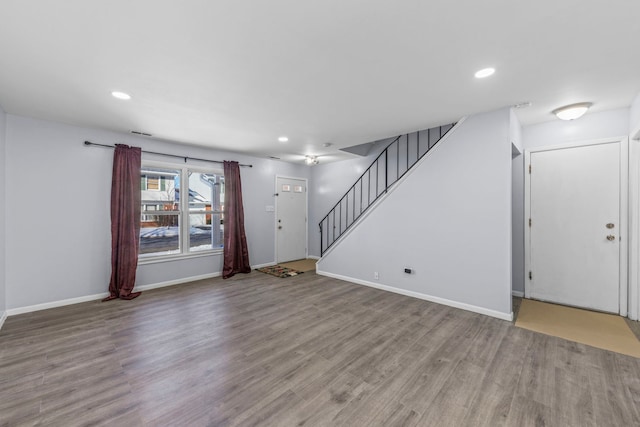 unfurnished living room featuring baseboards, stairway, and wood finished floors