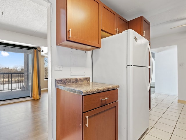 kitchen featuring light tile patterned floors, baseboards, brown cabinetry, and freestanding refrigerator