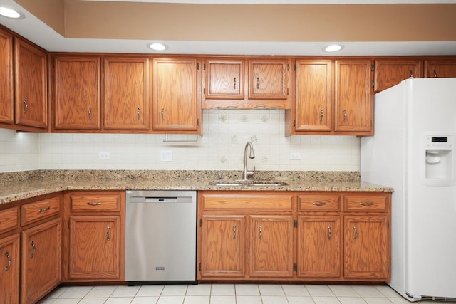 kitchen with white refrigerator with ice dispenser, dishwasher, backsplash, brown cabinets, and a sink