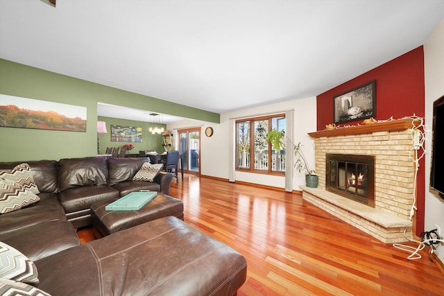 living room with a chandelier, a brick fireplace, light wood-style flooring, and baseboards