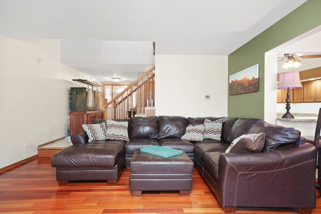 living area with stairs, ceiling fan, light wood-type flooring, and baseboards