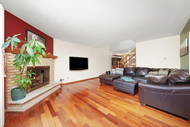 living room featuring light wood finished floors, stairs, a brick fireplace, and baseboards