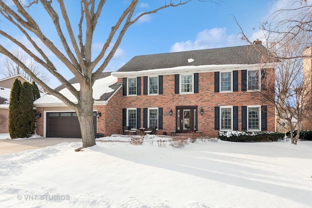 colonial-style house with a chimney, driveway, a garage, and brick siding