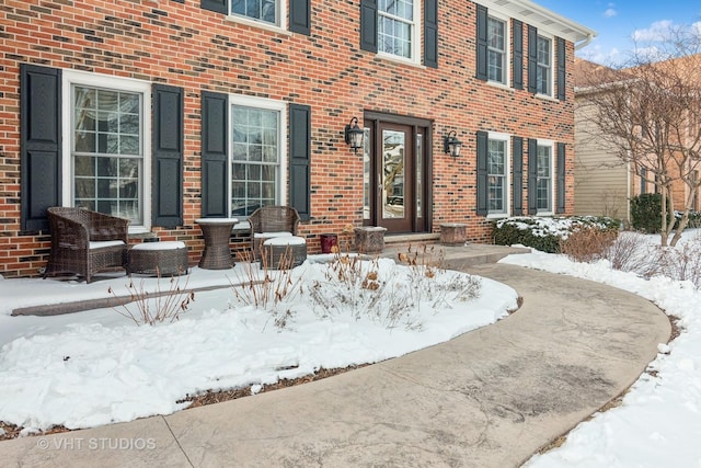 snow covered property entrance featuring brick siding