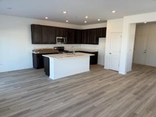 kitchen featuring dark brown cabinets, stove, an island with sink, light hardwood / wood-style floors, and sink