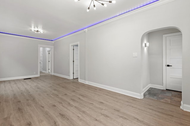 empty room featuring ornamental molding, baseboards, arched walkways, visible vents, and wood finished floors