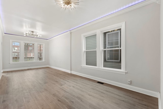 unfurnished room with an inviting chandelier, ornamental molding, baseboards, visible vents, and wood finished floors