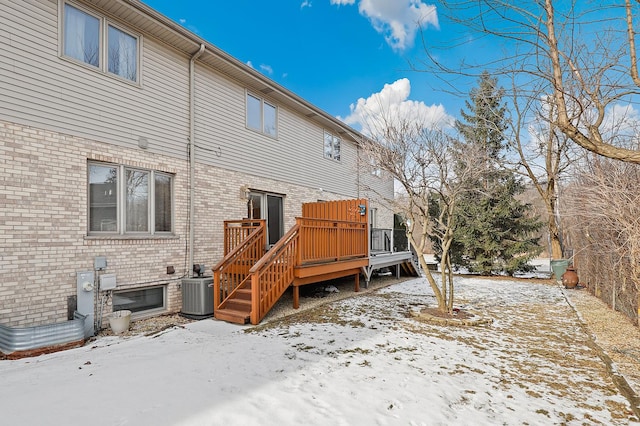 snow covered back of property featuring brick siding, a wooden deck, and central AC unit