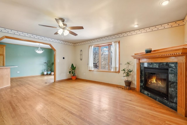 unfurnished living room with arched walkways, ceiling fan, a fireplace, baseboards, and light wood finished floors