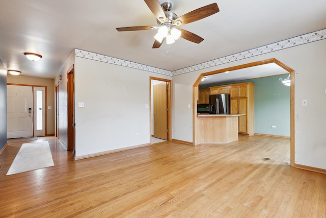 unfurnished living room featuring arched walkways, baseboards, a ceiling fan, and light wood-style floors