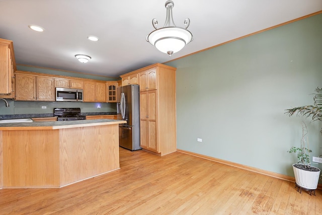 kitchen with appliances with stainless steel finishes, glass insert cabinets, a peninsula, light wood-style floors, and a sink