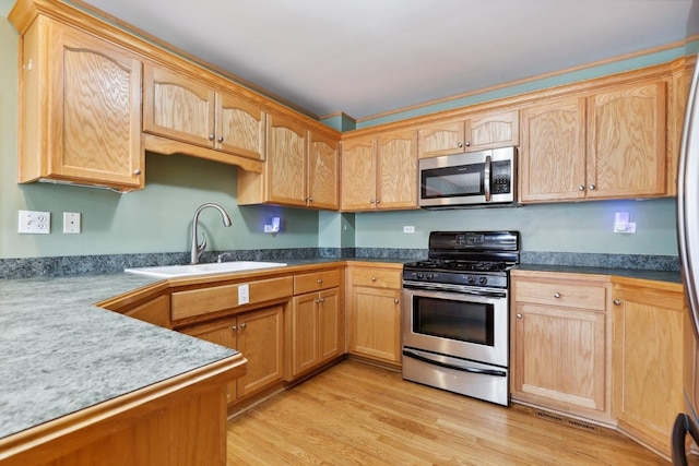 kitchen with stainless steel appliances, light wood-type flooring, a sink, and light brown cabinetry