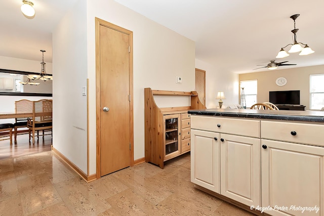 kitchen featuring baseboards, dark countertops, open floor plan, hanging light fixtures, and ceiling fan with notable chandelier