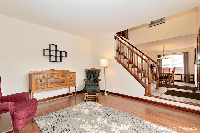 sitting room with an inviting chandelier, stairs, baseboards, and wood finished floors