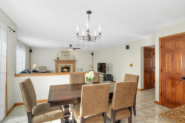 dining space with ceiling fan with notable chandelier and a brick fireplace