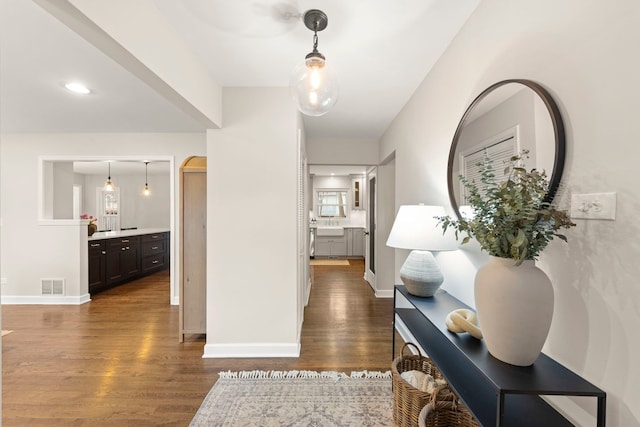 hall with arched walkways, dark wood-style flooring, visible vents, and baseboards