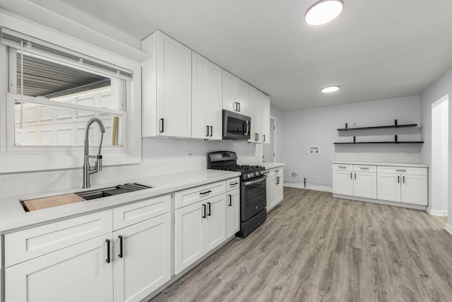 kitchen with sink, black gas range oven, white cabinets, and light hardwood / wood-style floors