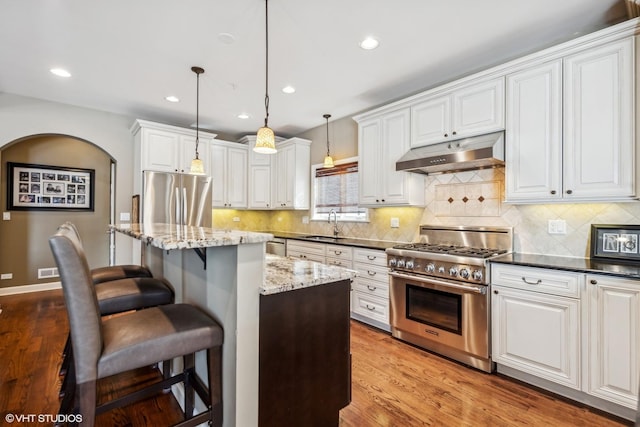 kitchen with a center island, pendant lighting, stainless steel appliances, dark stone countertops, and under cabinet range hood