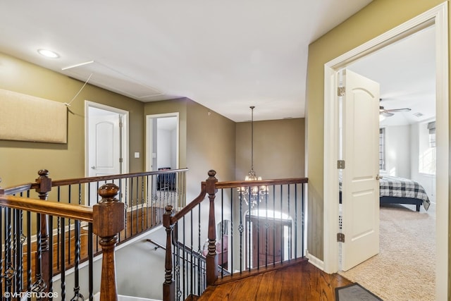 hall with baseboards, wood finished floors, a notable chandelier, and an upstairs landing