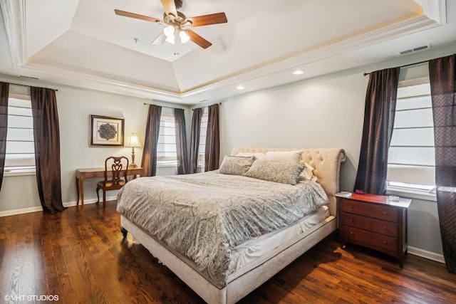 bedroom featuring visible vents, a tray ceiling, dark wood finished floors, and baseboards