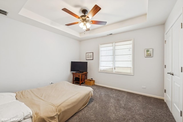 bedroom featuring a tray ceiling, baseboards, visible vents, and dark colored carpet